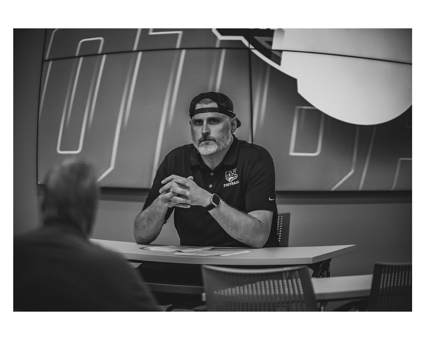 Coach Garner mid-conversation in a film-room setting, black and white.